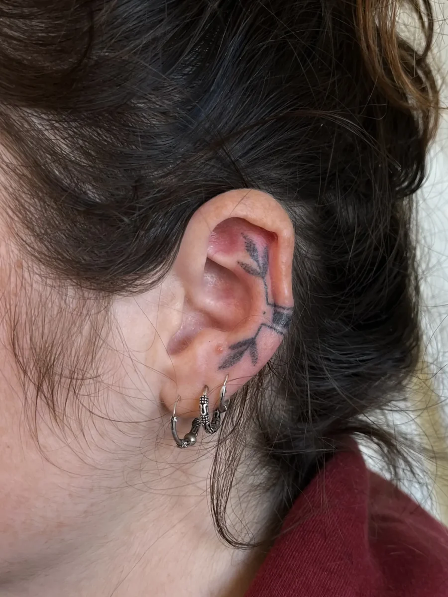 Tatouage handpoke ornemental autour de l’oreille, réalisé par Flori Green